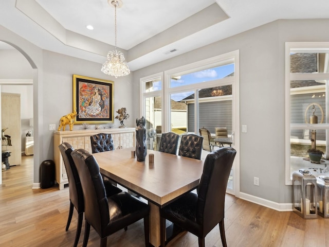 dining area with a raised ceiling, a chandelier, and light wood-type flooring