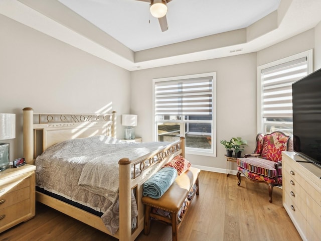 bedroom featuring ceiling fan, multiple windows, light hardwood / wood-style floors, and a raised ceiling