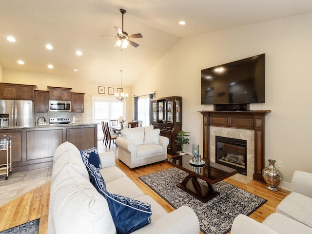 living room with a tiled fireplace, light wood-type flooring, lofted ceiling, and ceiling fan with notable chandelier