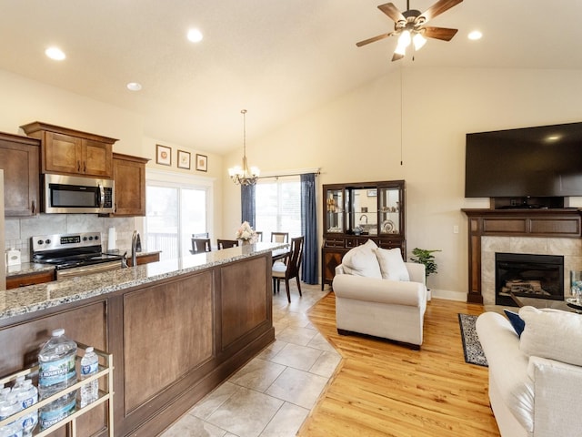 kitchen with a tiled fireplace, stainless steel appliances, light stone counters, decorative backsplash, and decorative light fixtures