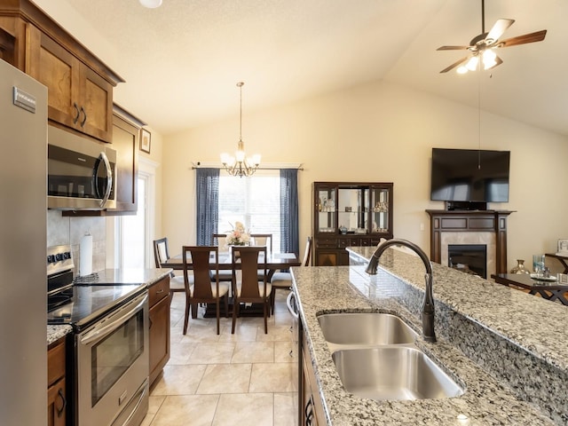 kitchen featuring a tile fireplace, appliances with stainless steel finishes, sink, lofted ceiling, and ceiling fan with notable chandelier