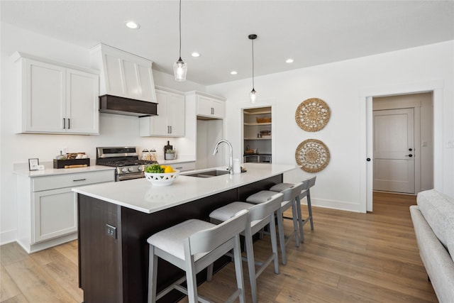 kitchen with a kitchen island with sink, pendant lighting, a kitchen bar, stainless steel range with gas cooktop, and white cabinets