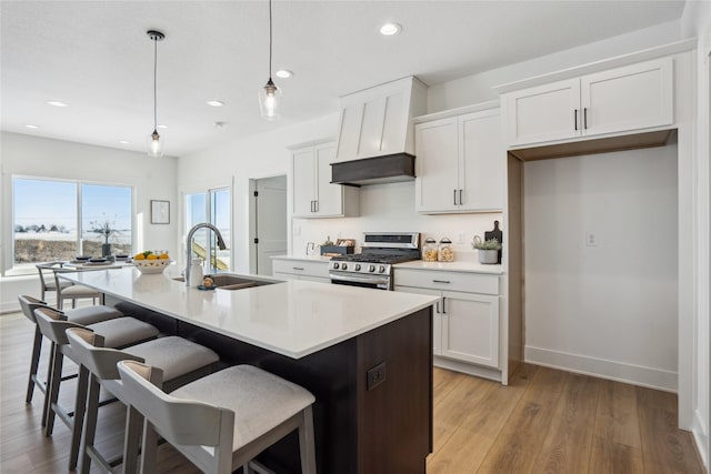 kitchen with a kitchen island with sink, hanging light fixtures, sink, white cabinetry, and gas range