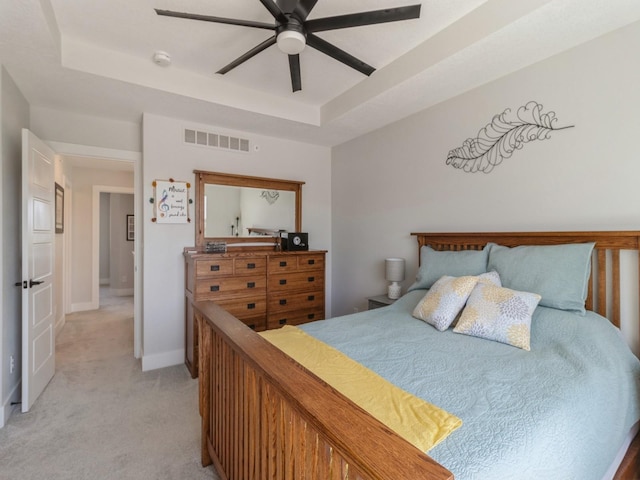 bedroom with a raised ceiling, ceiling fan, and light colored carpet