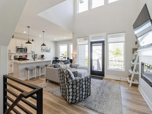 living room featuring sink, light hardwood / wood-style flooring, and a high ceiling