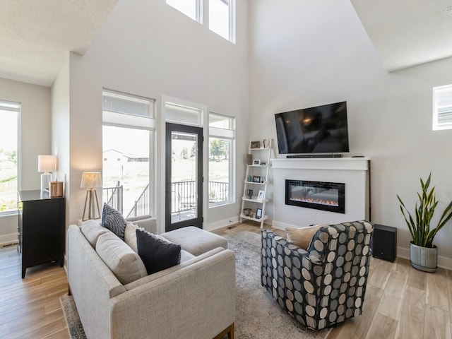 living room with light hardwood / wood-style floors, a towering ceiling, and plenty of natural light