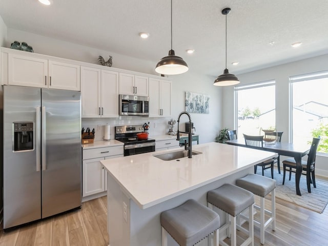 kitchen with a center island with sink, appliances with stainless steel finishes, pendant lighting, sink, and white cabinetry