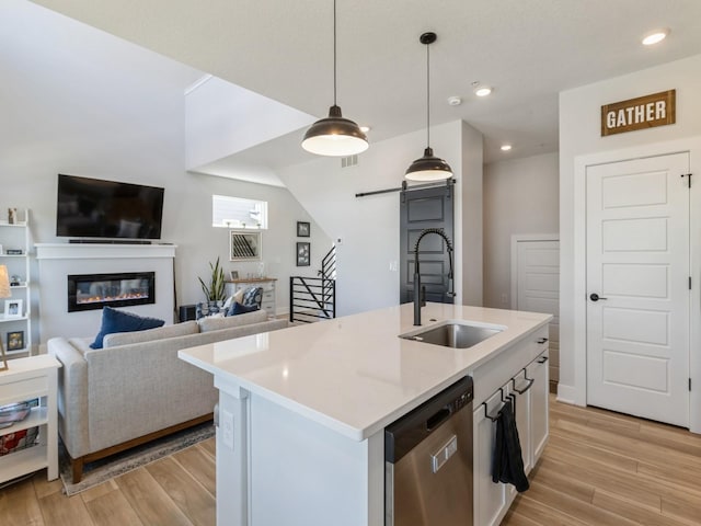 kitchen with a center island with sink, hanging light fixtures, sink, white cabinetry, and stainless steel dishwasher