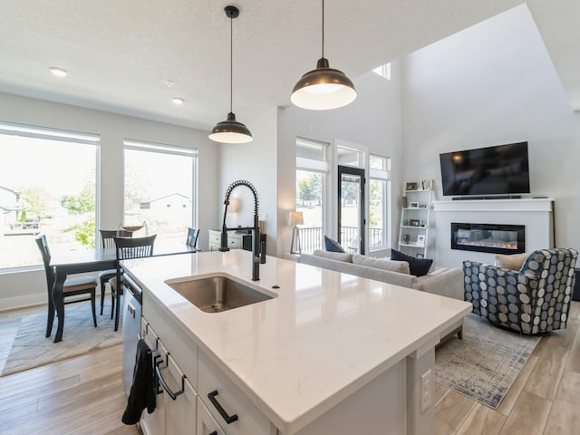 kitchen featuring light stone counters, hanging light fixtures, an island with sink, light wood-type flooring, and sink