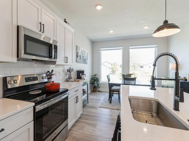 kitchen featuring appliances with stainless steel finishes, hanging light fixtures, white cabinets, backsplash, and sink