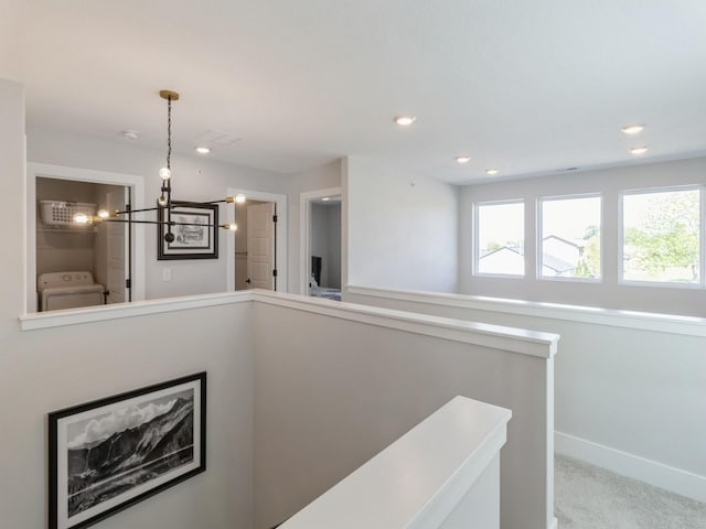 hall featuring washer / clothes dryer, an inviting chandelier, and light carpet