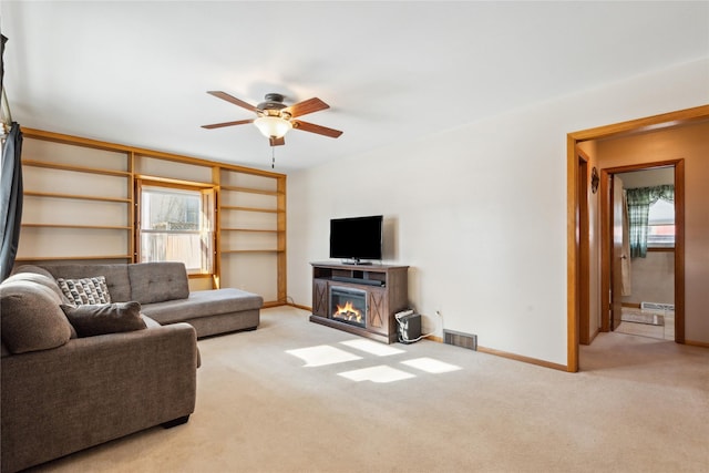 living room with a fireplace, light carpet, and ceiling fan