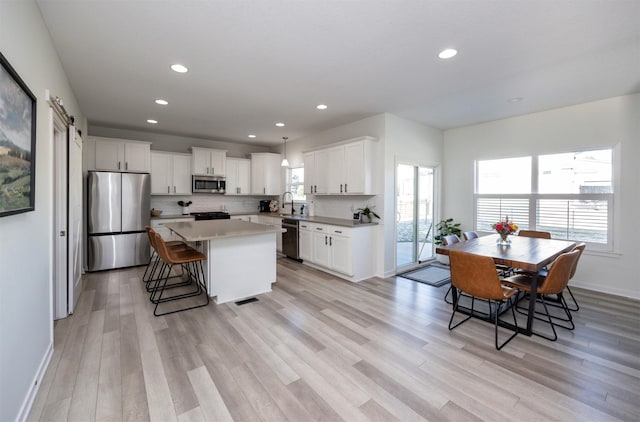 kitchen with stainless steel appliances, white cabinetry, a barn door, and a kitchen island