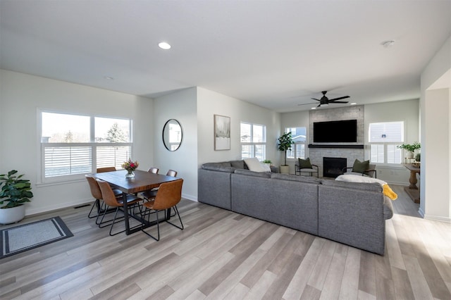 living room featuring ceiling fan, light wood-type flooring, a stone fireplace, and a wealth of natural light