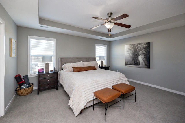 bedroom with ceiling fan, light carpet, and a tray ceiling