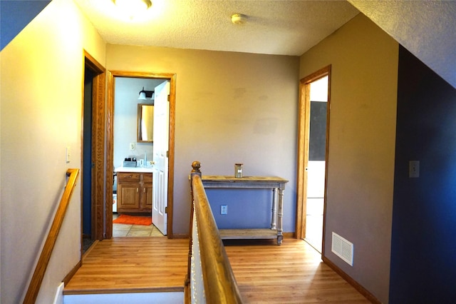 corridor with light wood-type flooring and a textured ceiling