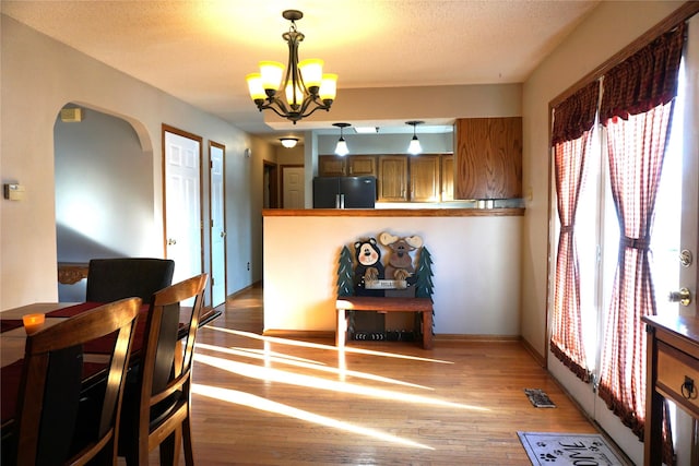 dining room featuring a textured ceiling, a notable chandelier, and light wood-type flooring