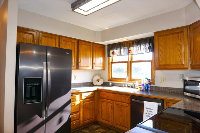 kitchen featuring brown cabinets, dark countertops, a sink, and appliances with stainless steel finishes