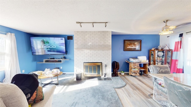 living room with a fireplace, track lighting, a textured ceiling, and light hardwood / wood-style flooring