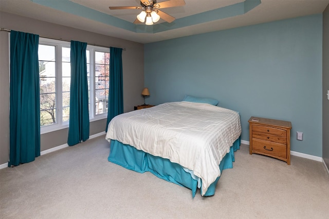 bedroom featuring ceiling fan, light colored carpet, a tray ceiling, and multiple windows