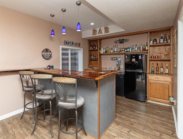 bar featuring decorative light fixtures, black fridge, butcher block countertops, wood-type flooring, and a textured ceiling