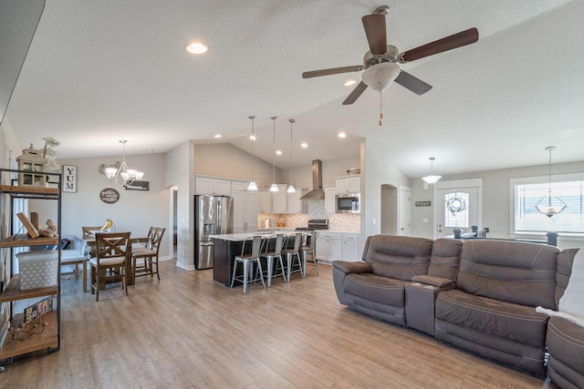 living room with lofted ceiling, ceiling fan with notable chandelier, and light hardwood / wood-style flooring