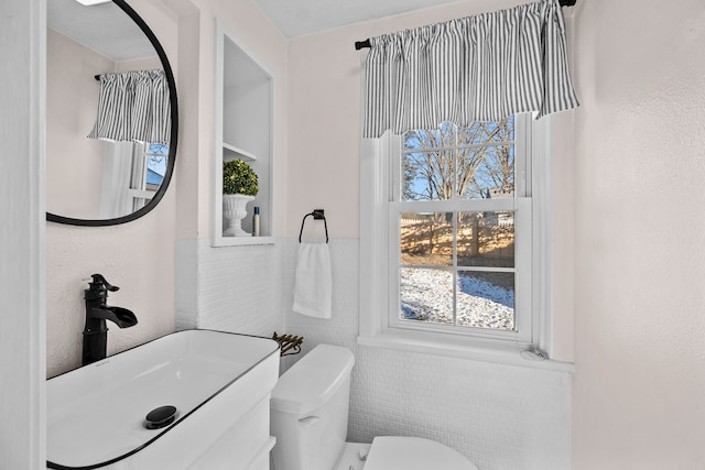 bathroom with toilet, tile walls, and sink