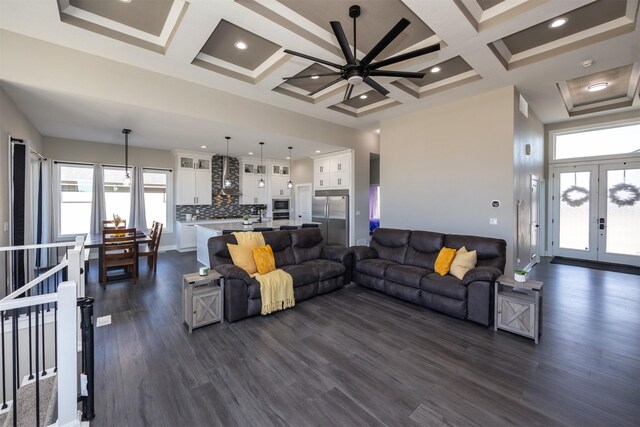 living room featuring a towering ceiling, beamed ceiling, dark hardwood / wood-style floors, ceiling fan, and coffered ceiling