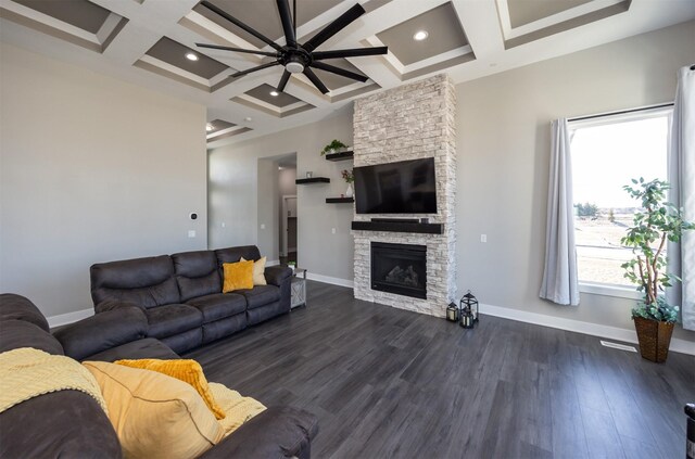 living room featuring dark hardwood / wood-style floors, coffered ceiling, a stone fireplace, and beamed ceiling