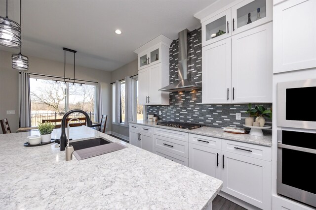 kitchen with pendant lighting, white cabinets, wall chimney range hood, sink, and stainless steel gas cooktop