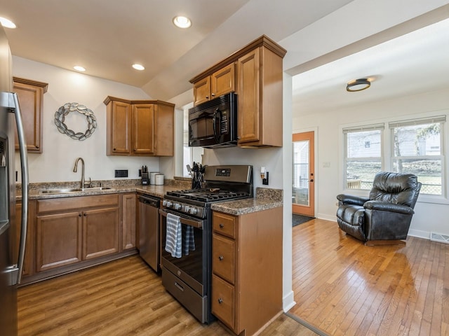 kitchen featuring vaulted ceiling, sink, light hardwood / wood-style flooring, stainless steel appliances, and dark stone counters