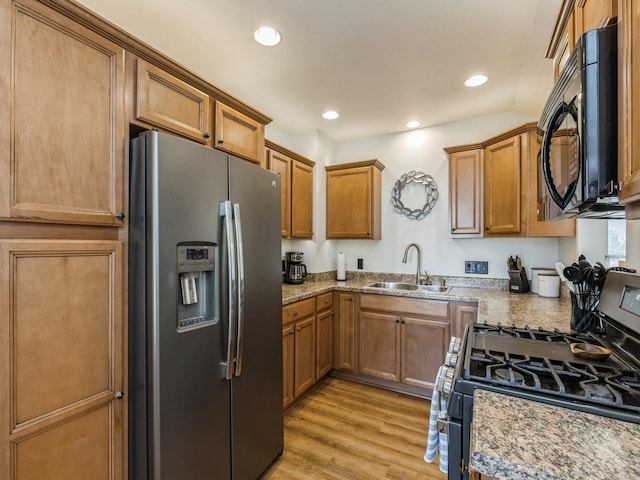 kitchen featuring light stone countertops, appliances with stainless steel finishes, light wood-type flooring, sink, and vaulted ceiling