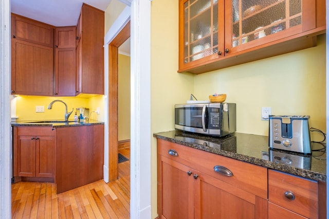 kitchen with sink, dark stone countertops, crown molding, and light hardwood / wood-style floors