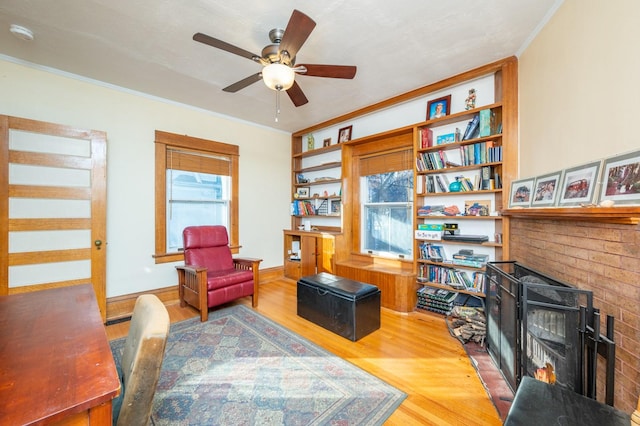 living area featuring ceiling fan, a fireplace, crown molding, and hardwood / wood-style flooring