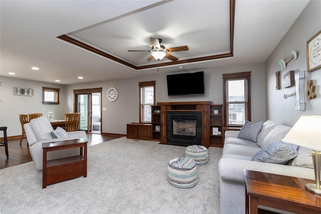 carpeted living room with ceiling fan, a tray ceiling, and ornamental molding