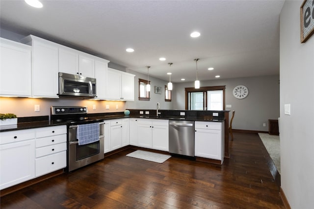 kitchen with white cabinets, appliances with stainless steel finishes, decorative light fixtures, dark wood-type flooring, and kitchen peninsula