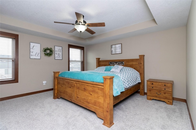 bedroom with a raised ceiling, ceiling fan, light carpet, and multiple windows