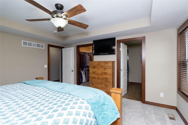 carpeted bedroom with ceiling fan, a walk in closet, a closet, and a raised ceiling