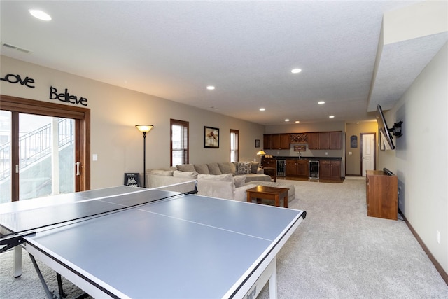 rec room featuring light carpet, a textured ceiling, and beverage cooler