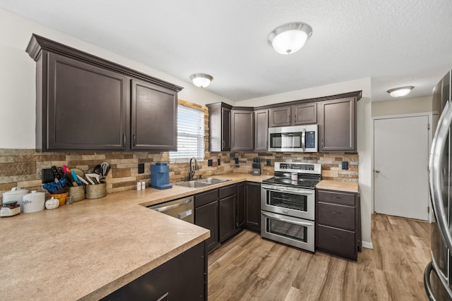 kitchen with appliances with stainless steel finishes, sink, decorative backsplash, dark brown cabinetry, and light wood-type flooring