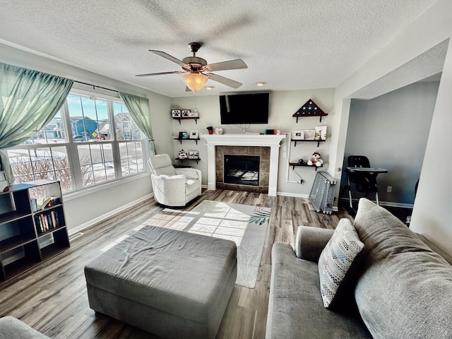 living room featuring a ceiling fan, a tile fireplace, baseboards, and wood finished floors