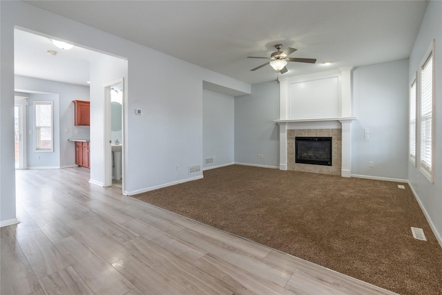 unfurnished living room featuring light carpet, ceiling fan, and a tile fireplace