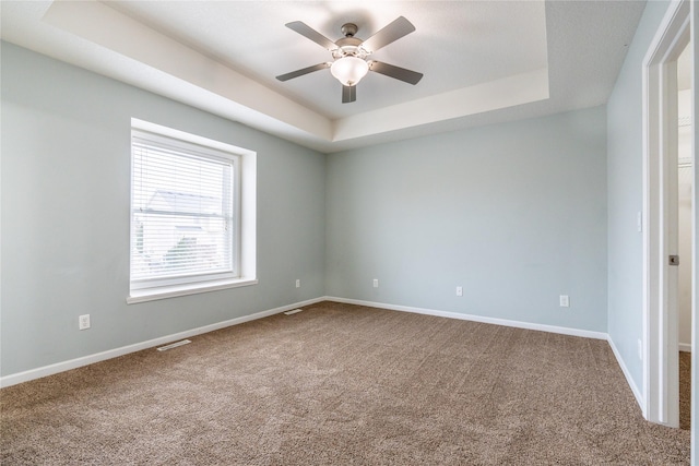 spare room with ceiling fan, a wealth of natural light, a raised ceiling, and carpet flooring