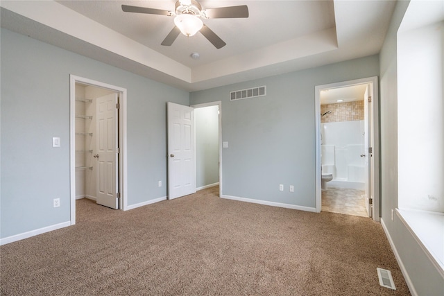 unfurnished bedroom with ensuite bath, ceiling fan, a spacious closet, and a raised ceiling