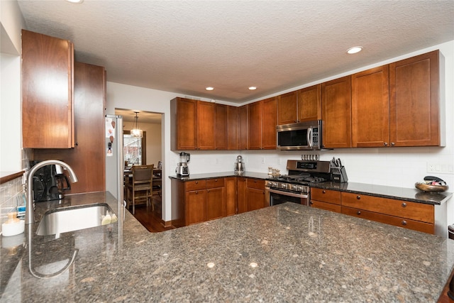 kitchen featuring kitchen peninsula, appliances with stainless steel finishes, dark stone countertops, a textured ceiling, and sink