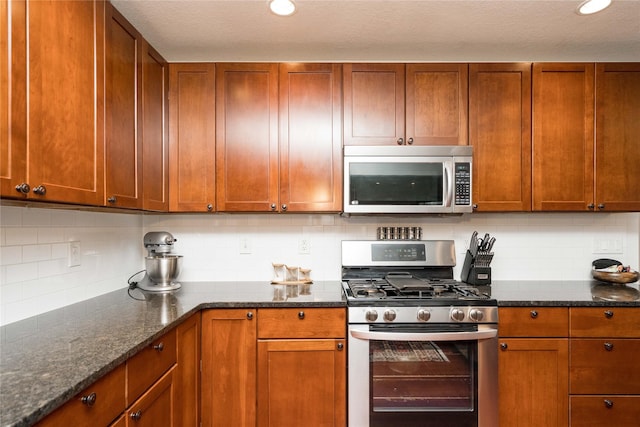 kitchen with a textured ceiling, stainless steel appliances, dark stone countertops, and backsplash