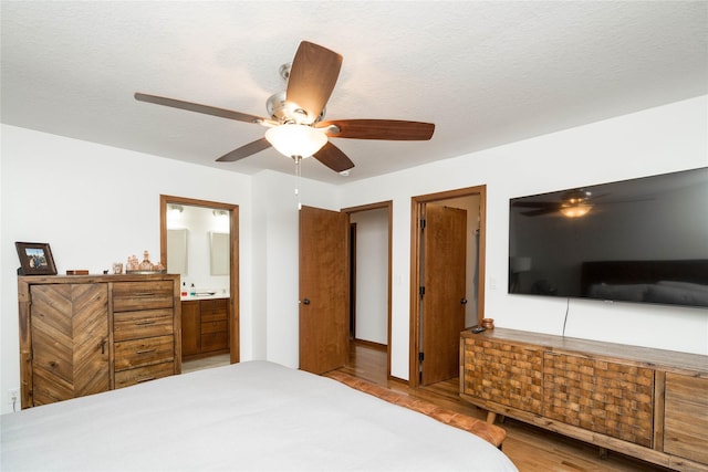 bedroom featuring ceiling fan, light wood-type flooring, connected bathroom, and a textured ceiling