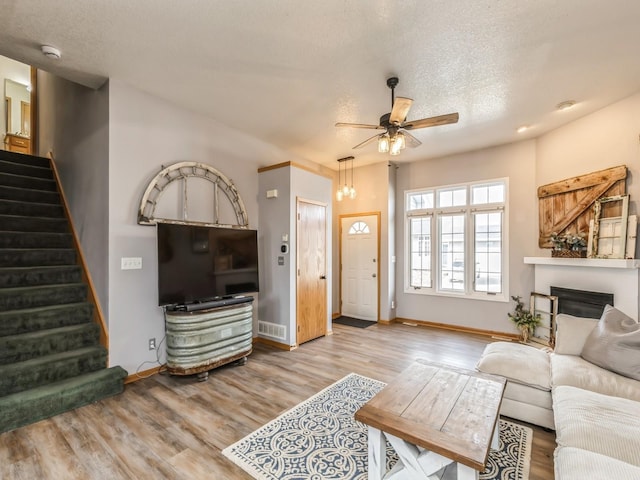 living room with a textured ceiling, ceiling fan, and light hardwood / wood-style flooring