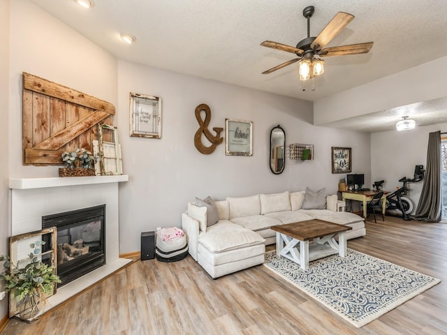 living room with ceiling fan, a tile fireplace, a textured ceiling, and light wood-type flooring