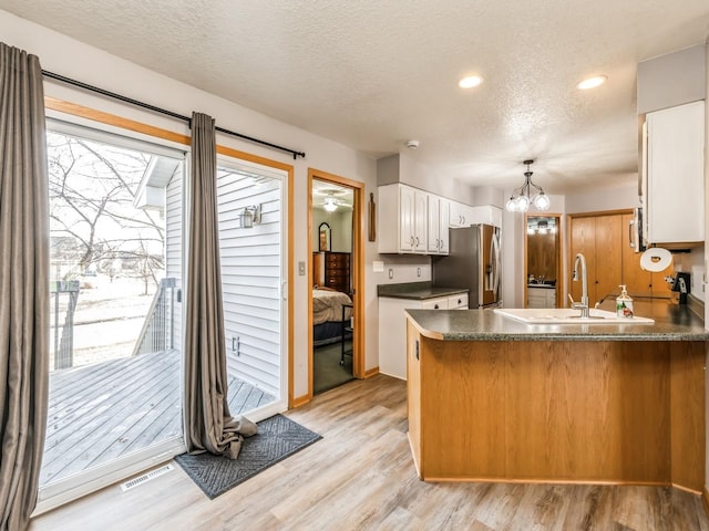 kitchen featuring sink, white cabinetry, stainless steel fridge, kitchen peninsula, and light hardwood / wood-style floors